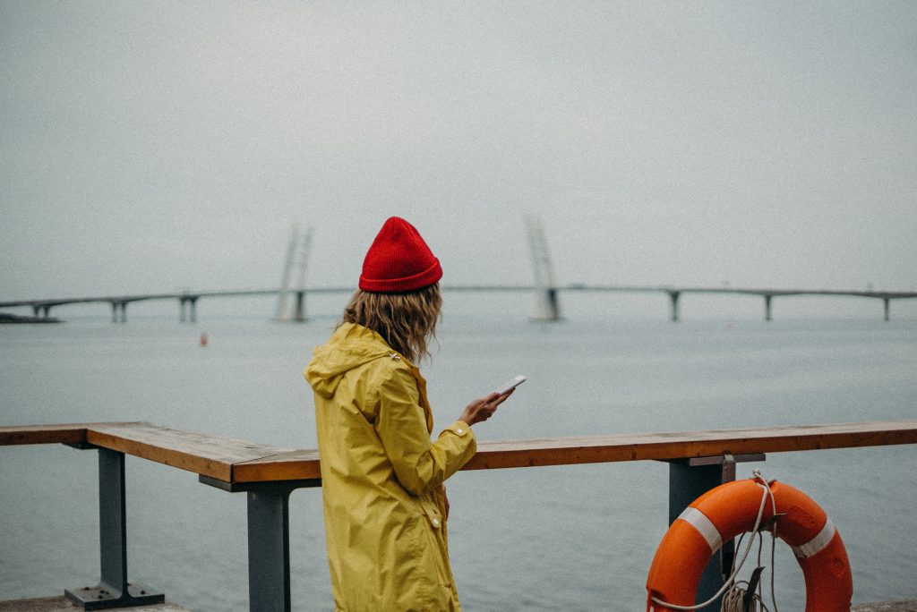 Female coach by sea on her phone, reflecting on her branding