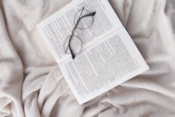 Kuscheldecke aus Fleece unter einem aufgeschlagenem Buch und einer abgesetzten Brille