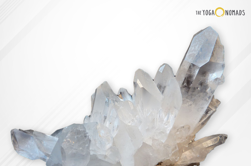 A cluster of clear quartz crystals with a translucent appearance and pointed terminations. The crystals are set against a light background that fades from white to beige.