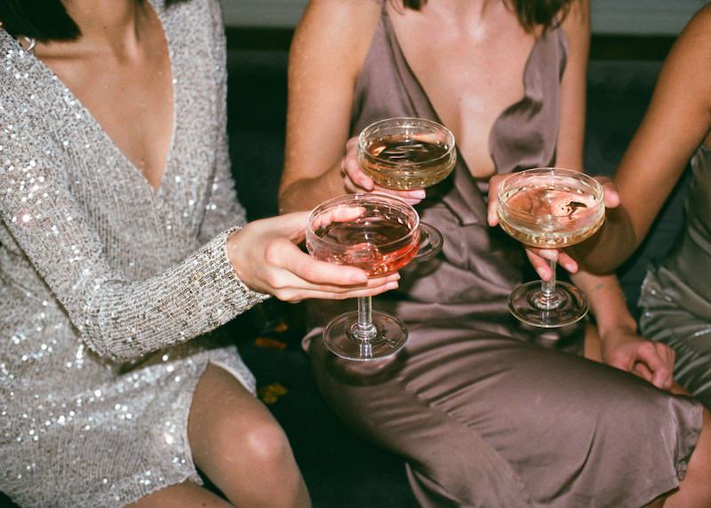 Drei Frauen in eleganten Abendkleidern sitzen und stoßen mit Sekt an
