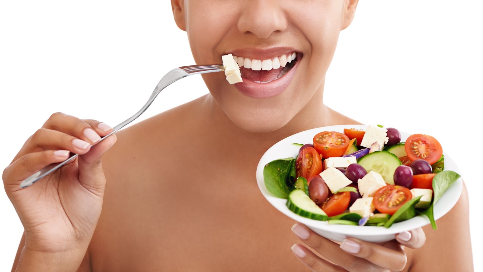 A cropped studio shot of a woman eating a salad against a white background, highlighting healthy food choices for maintaining strong teeth.