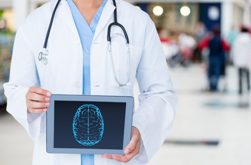 Fotografia de neurocirurgião com um jaleco e com um tablet na mão. O aparelho mostra o desenho de um cérebro.