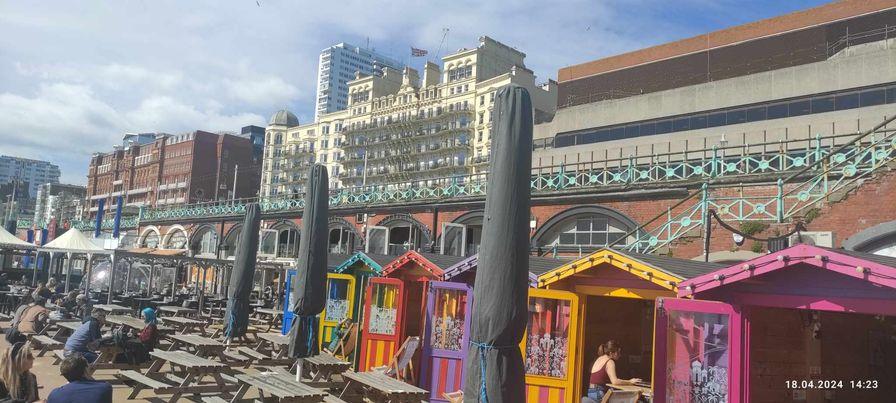 A group of colorful huts with umbrellas in front of a buildingDescription automatically generated