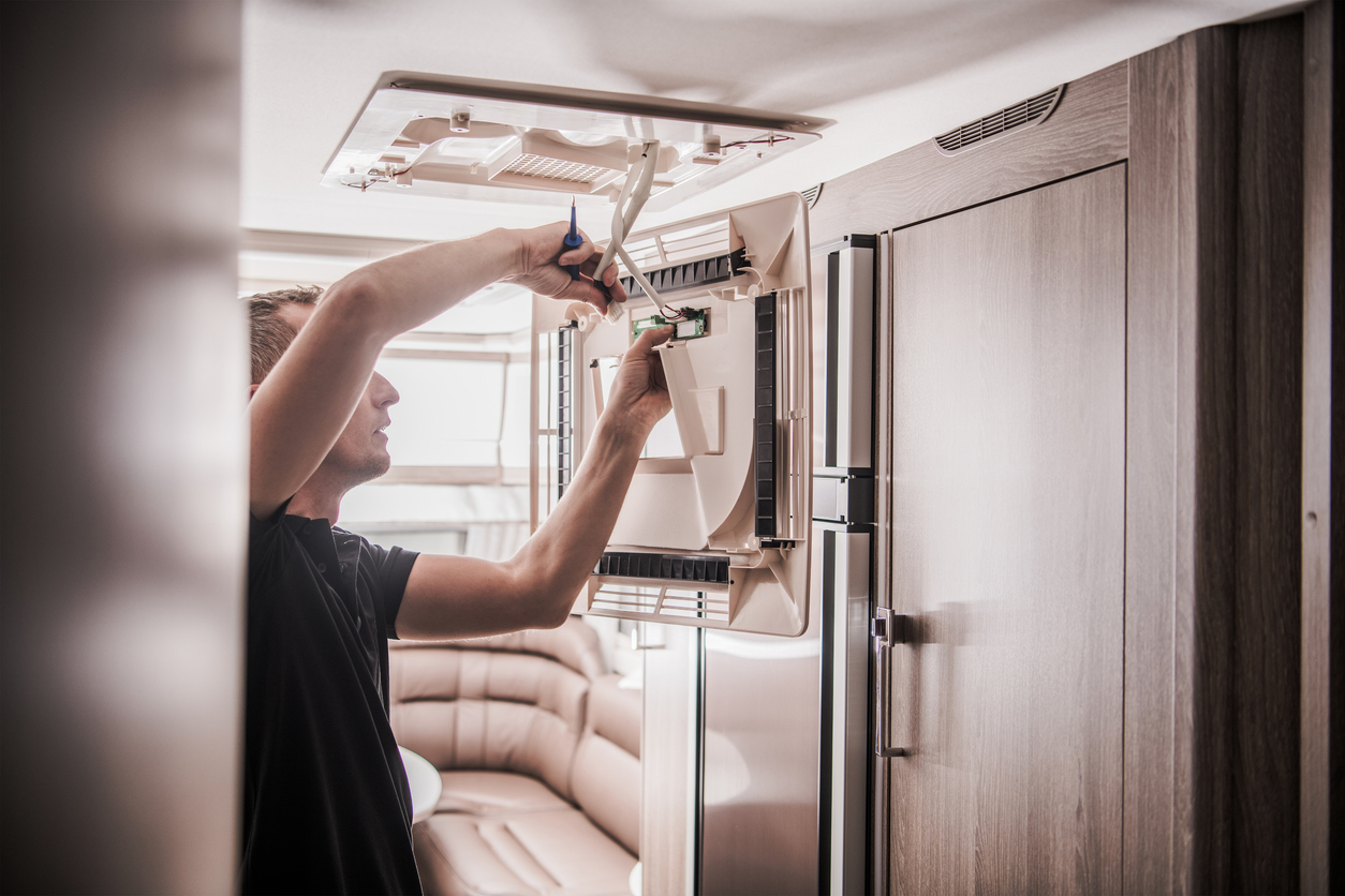 A side view of a man working to fix his RV’s air conditioner.  