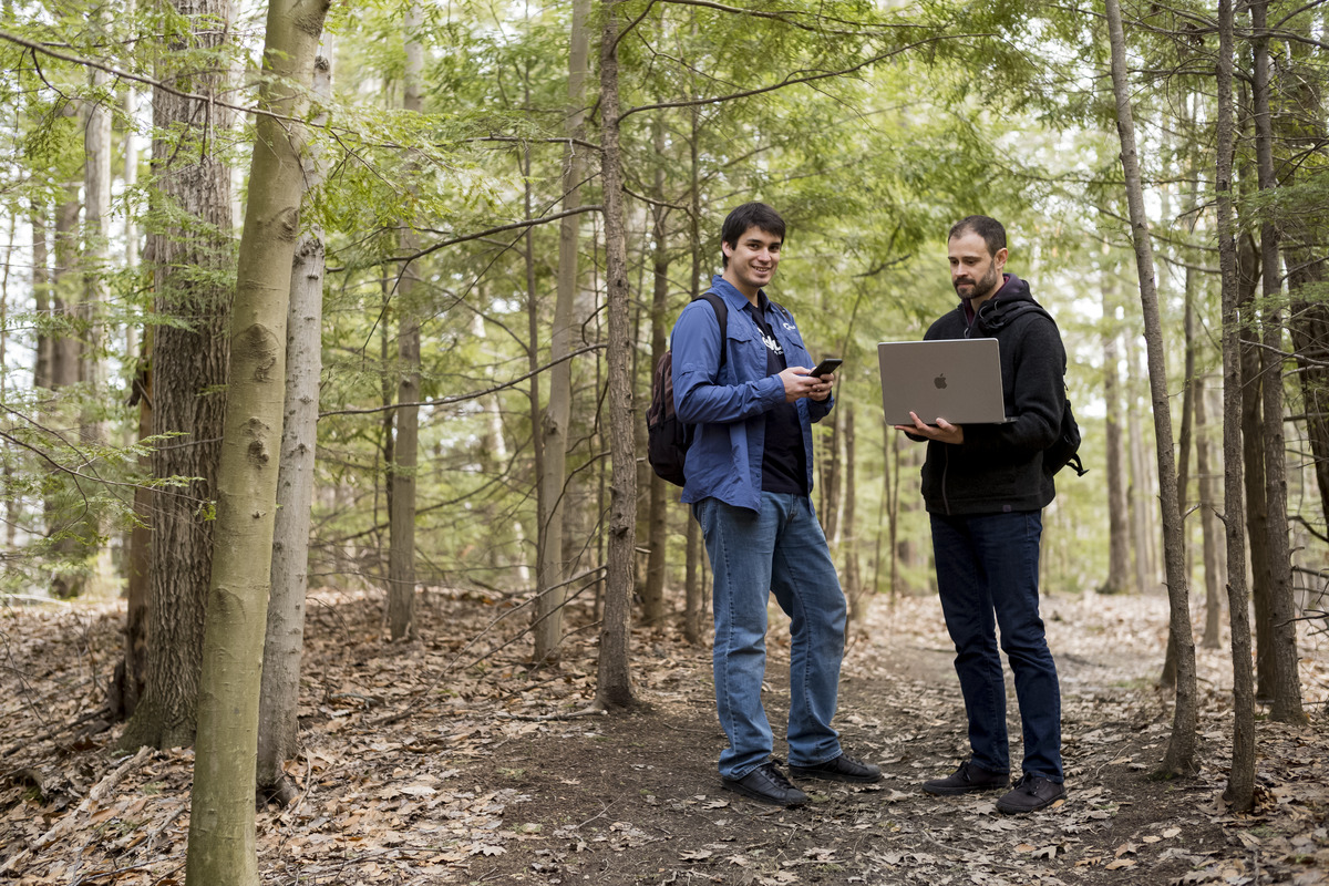 Men in the woods using phones and laptops. 