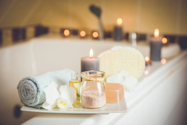 White ceramic tray with home spa supplies in home bathroom for relaxing rituals. Candlelight, salt soap bar, bath salt in jar, massage, bath oil in bottle, blue rolled towel, natural sponge. White ceramic tray with home spa supplies in home bathroom for relaxing rituals. Candlelight, salt soap bar, bath salt in jar, massage, bath oil in bottle, blue rolled towel, natural sponge. bath stock pictures, royalty-free photos & images