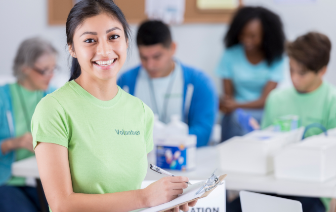 A woman volunteering for a fundraising event, while she wears a green t-shirt that says “volunteer” printed on the front.