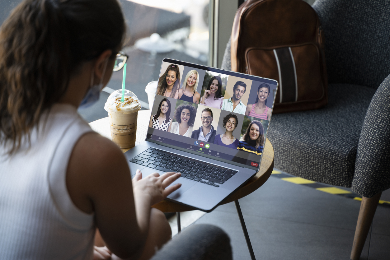 a woman talking to her team via a computer and while on a cafe