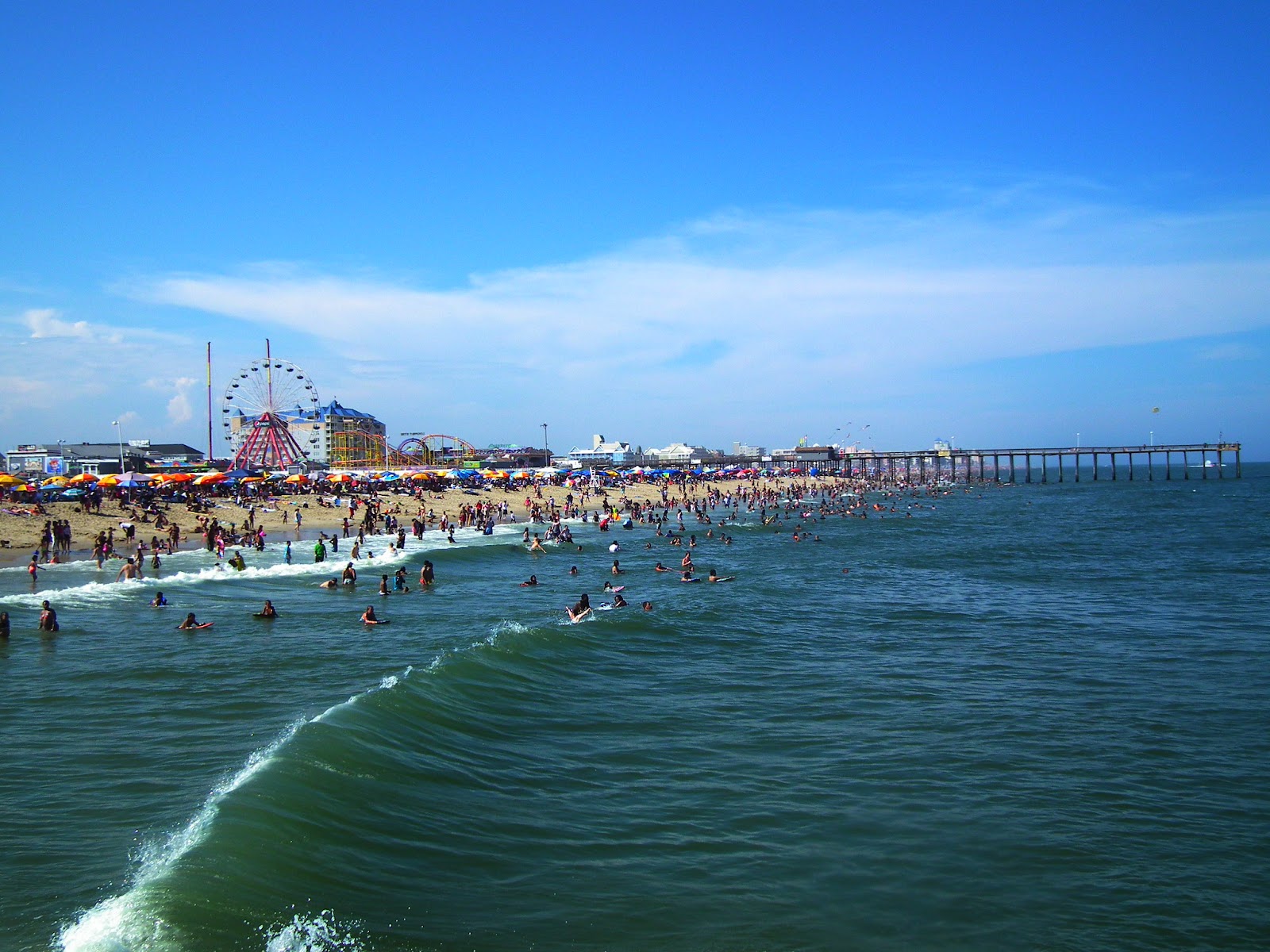 Gushing waves along the shore and people are enjoying on the beach, with a giant Ferris wheel in the background.