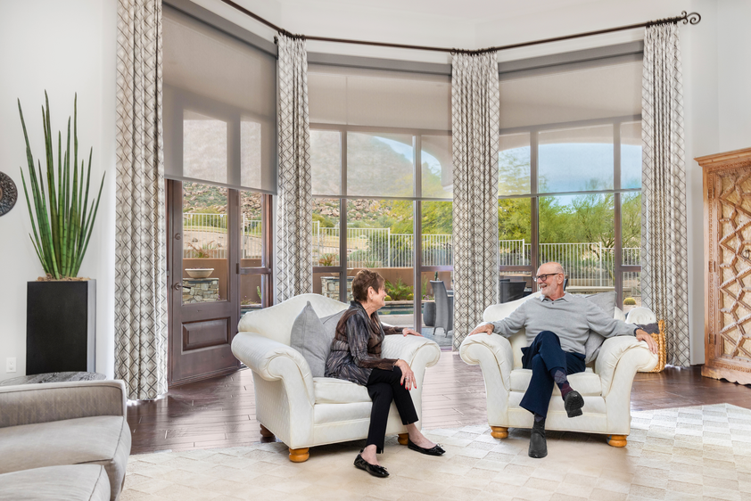 Couple sitting in their living room with linen curtains and roller shades in the background