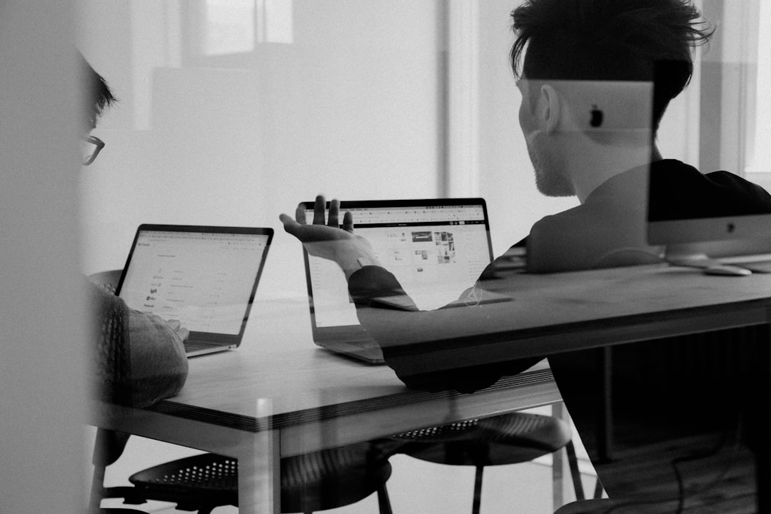 Two individuals working on laptops at a table, engaged in email marketing.