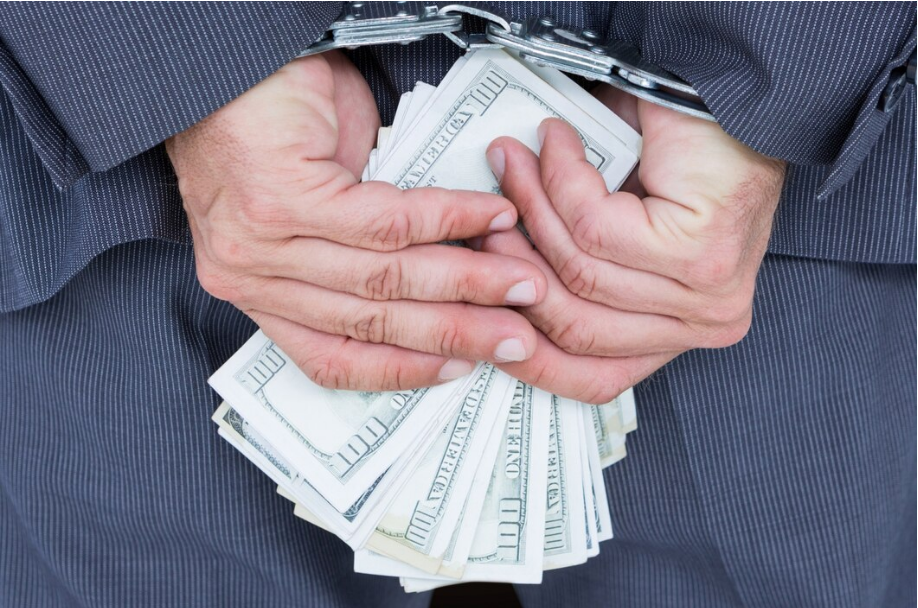 Man in handcuffs holding a stack of cash