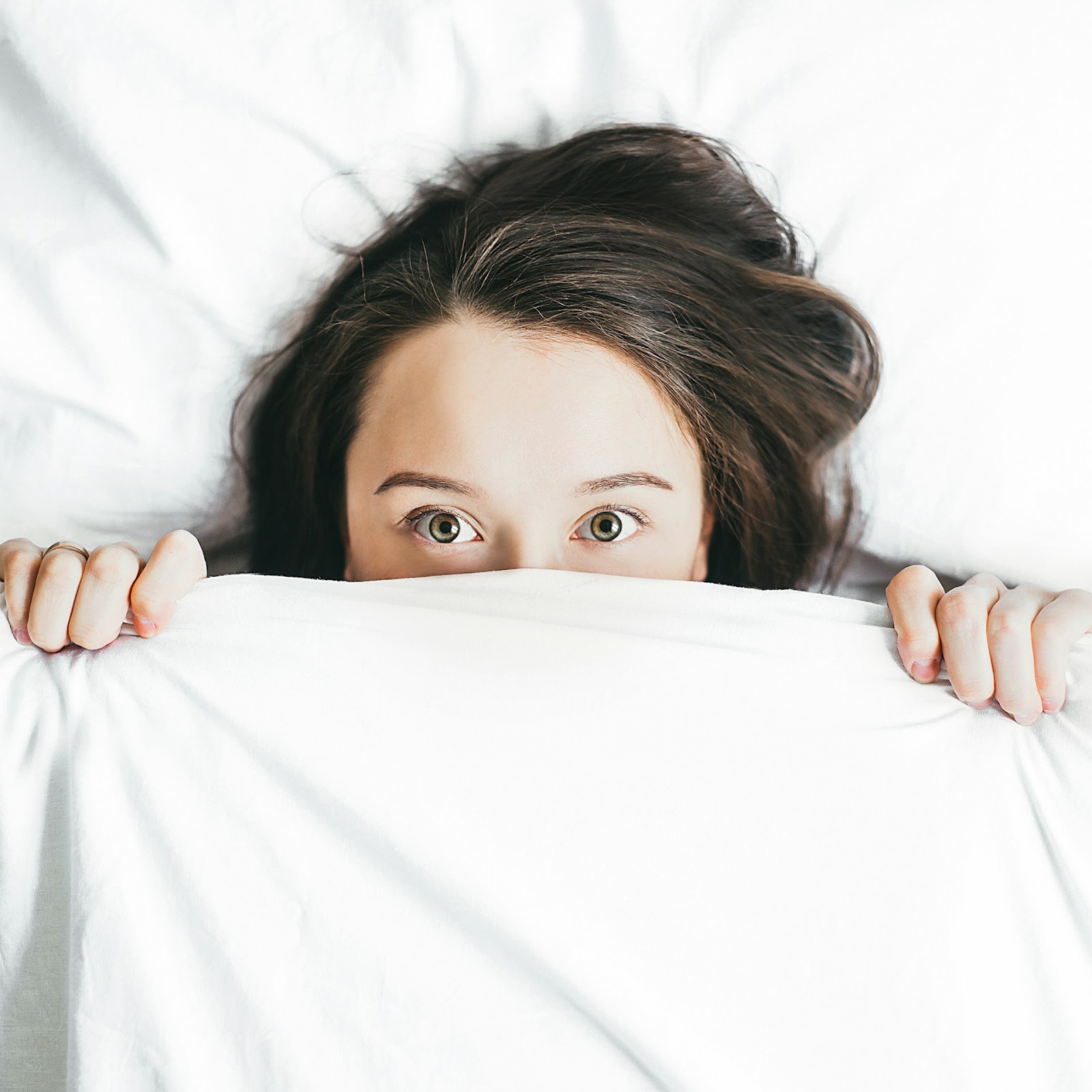 A woman peeking out from under a white sheet, looking curious and mysterious.