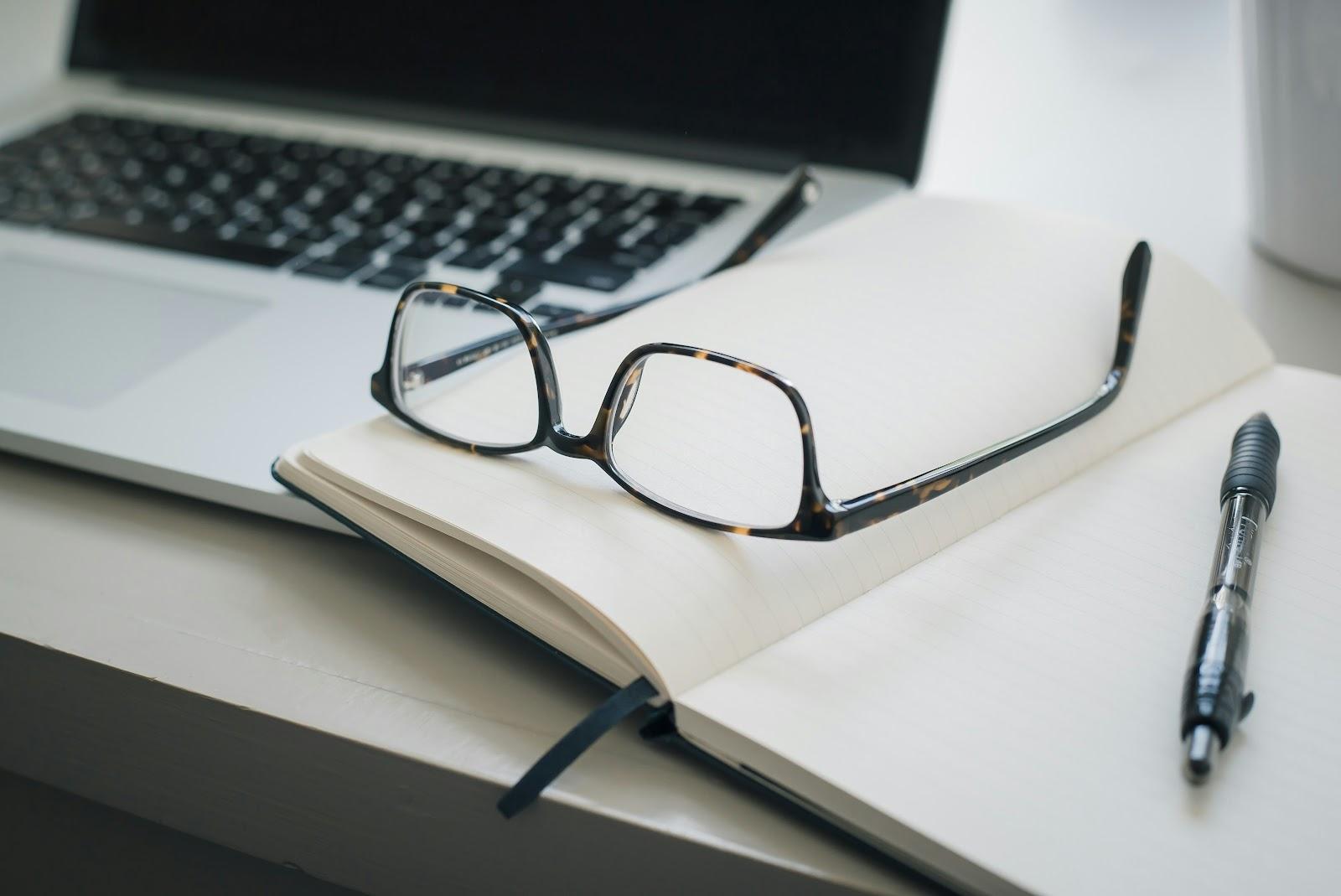 glasses on a notebook next to a laptop