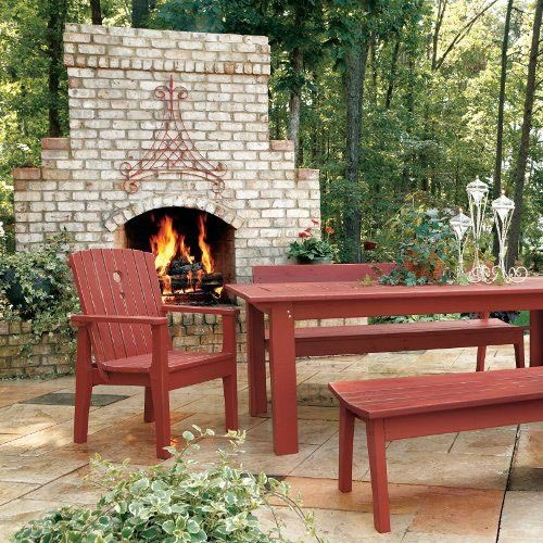 A large stone outdoor fireplace with red wooden furniture placed around it.
