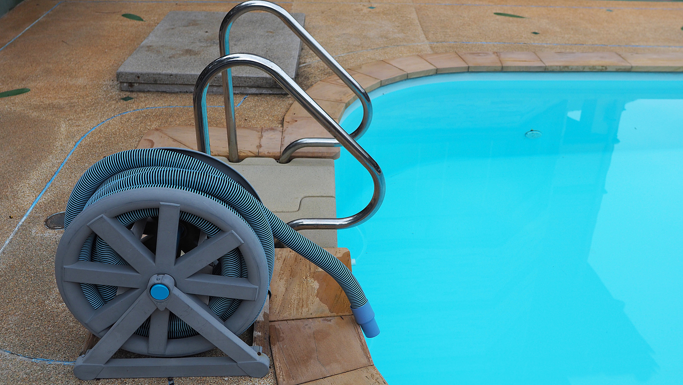 A swimming pool vacuum cleaner on concrete beside a backyard pool. 