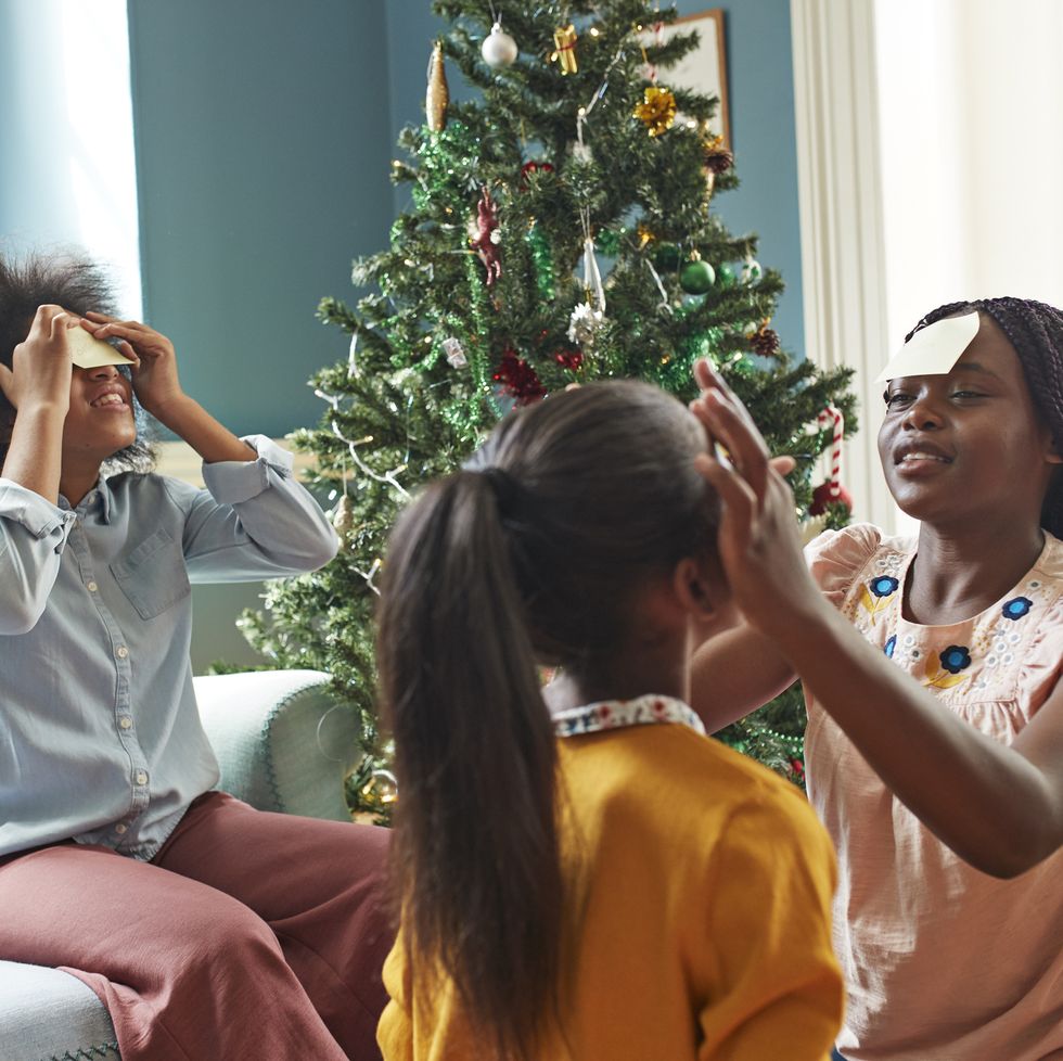 sisters sticking adhesive notes on forehead while sitting in living room at home during christmas