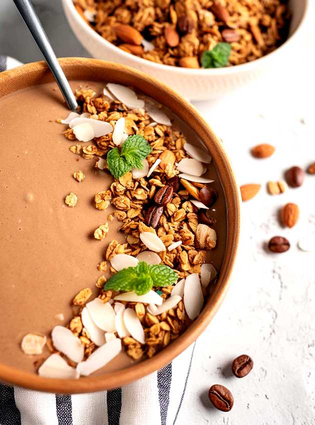 Coffee smoothie bowl topped with slivered almonds and granola, presented in a ceramic bowl on a striped tablecloth.