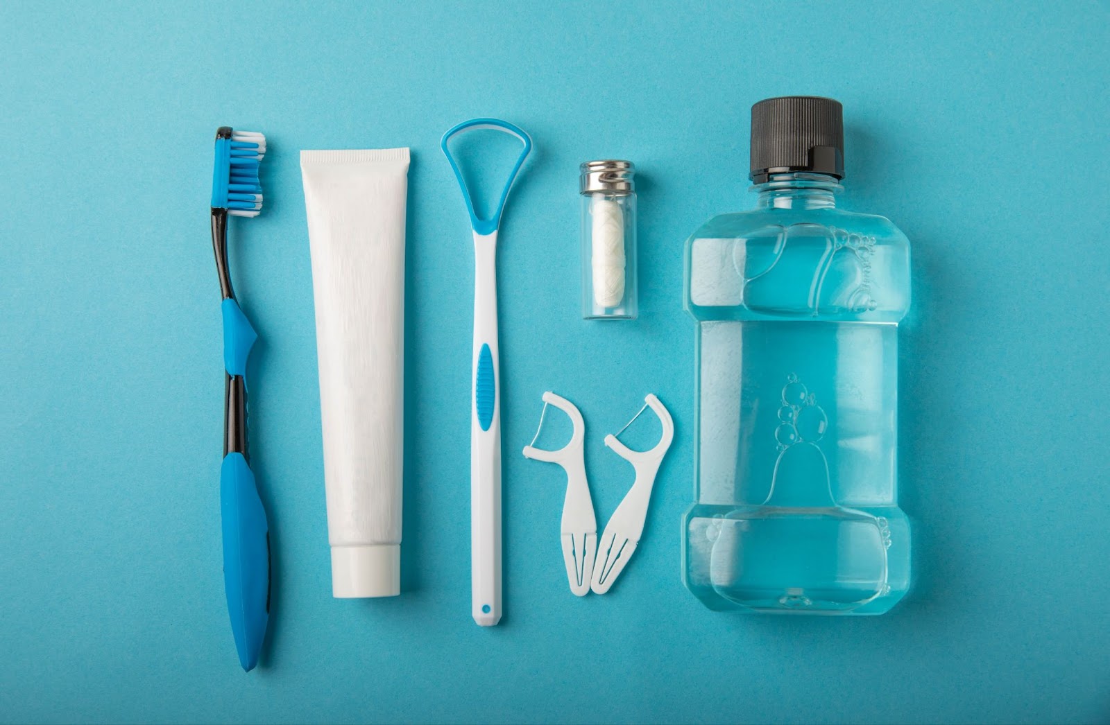 there is a tooth brush, tooth paste, tongue scraper, floss, and mouthwash against a blue background, all tools that can be used to prevent cavities.