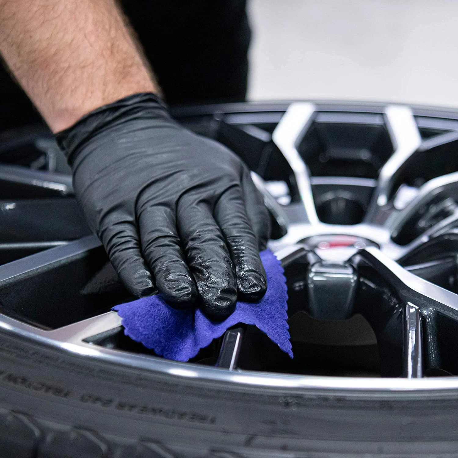 Hand in a black glove applying a final smoothing to a wheel with a blue microfiber cloth, part of the ceramic coating process for enhanced durability and shine.
