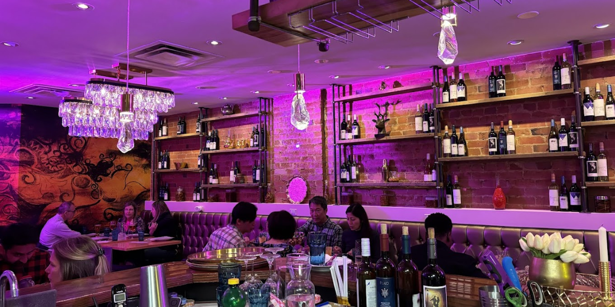 A dimly lit restaurant with purple ambiance, showcasing rows of wine bottles on display.