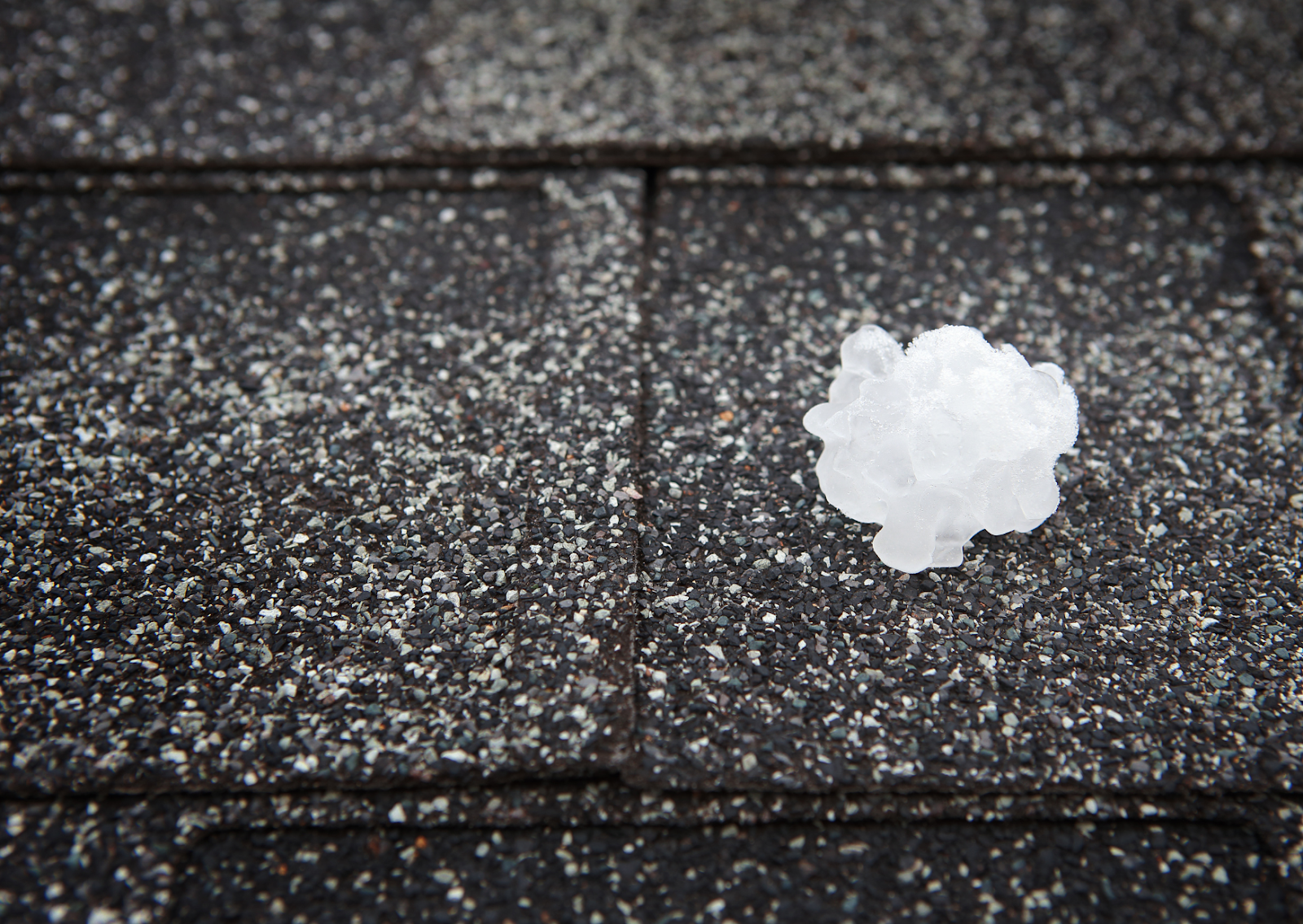 Large hailstone on a shingled surface, highlighting the potential for a hail-damaged roof after severe weather conditions.