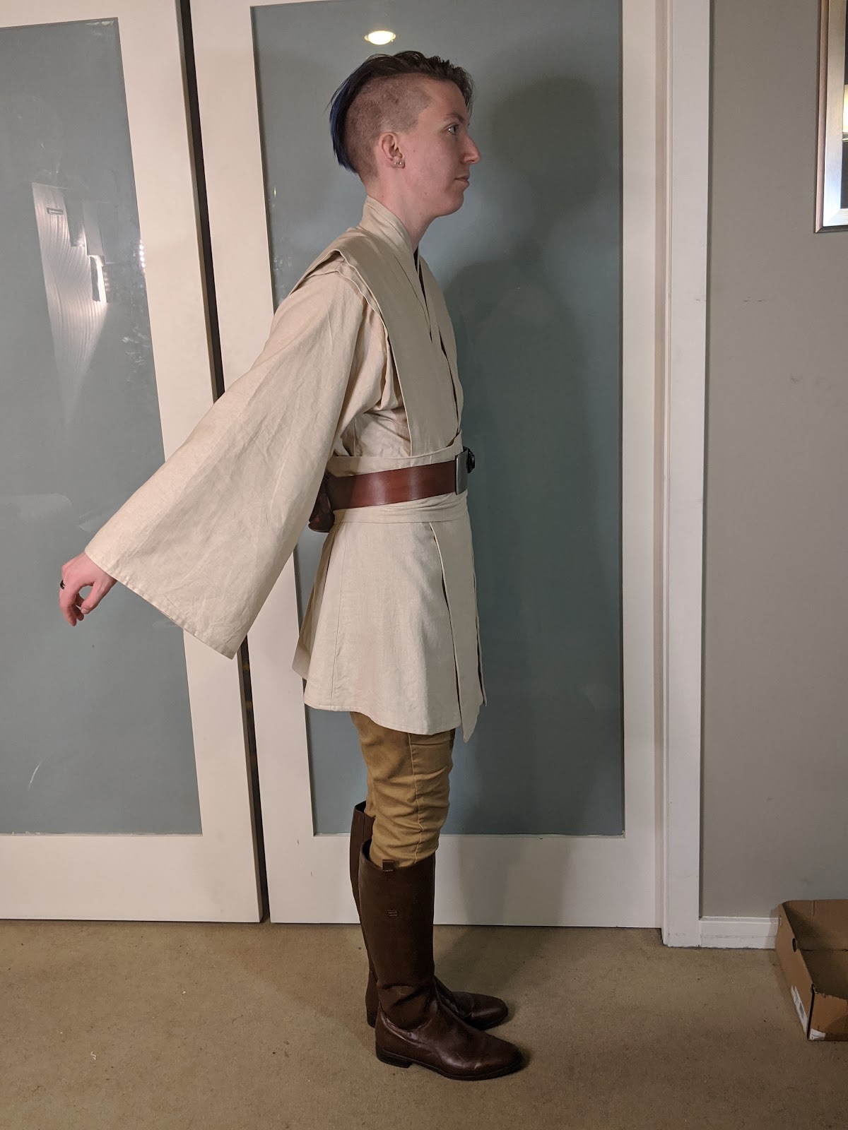 Image description: A person in a Jedi costume, facing towards the right, with their arms extended behind them. /end description