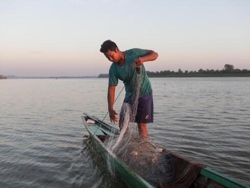 A fisher pulls a net into a boat in low light