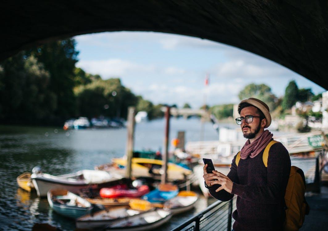 Free Man Holding Smartphone Near Boats Stock Photo