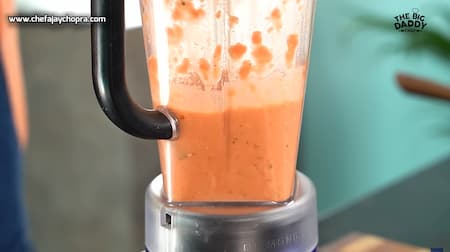Blender with freshly blended tomato and basil sauce, showing a smooth and vibrant red pizza sauce.