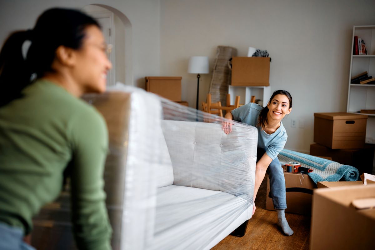 Two smiling women moving a couch into a new apartment.