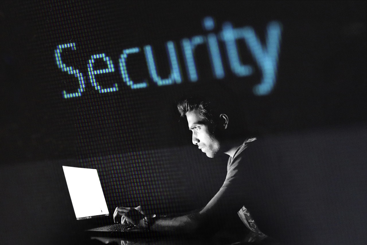 A person working on a laptop in the dark with "Security" displayed in the background.