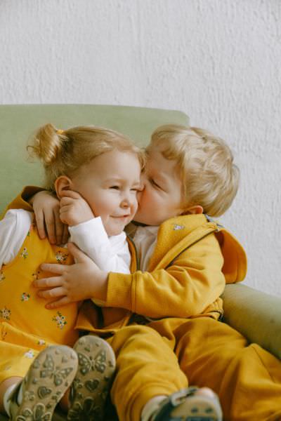 Zwei Kleinkinder auf einer grünen Couch schmusen mit ihren Lieblingspullis mit Bündchenabschluss.