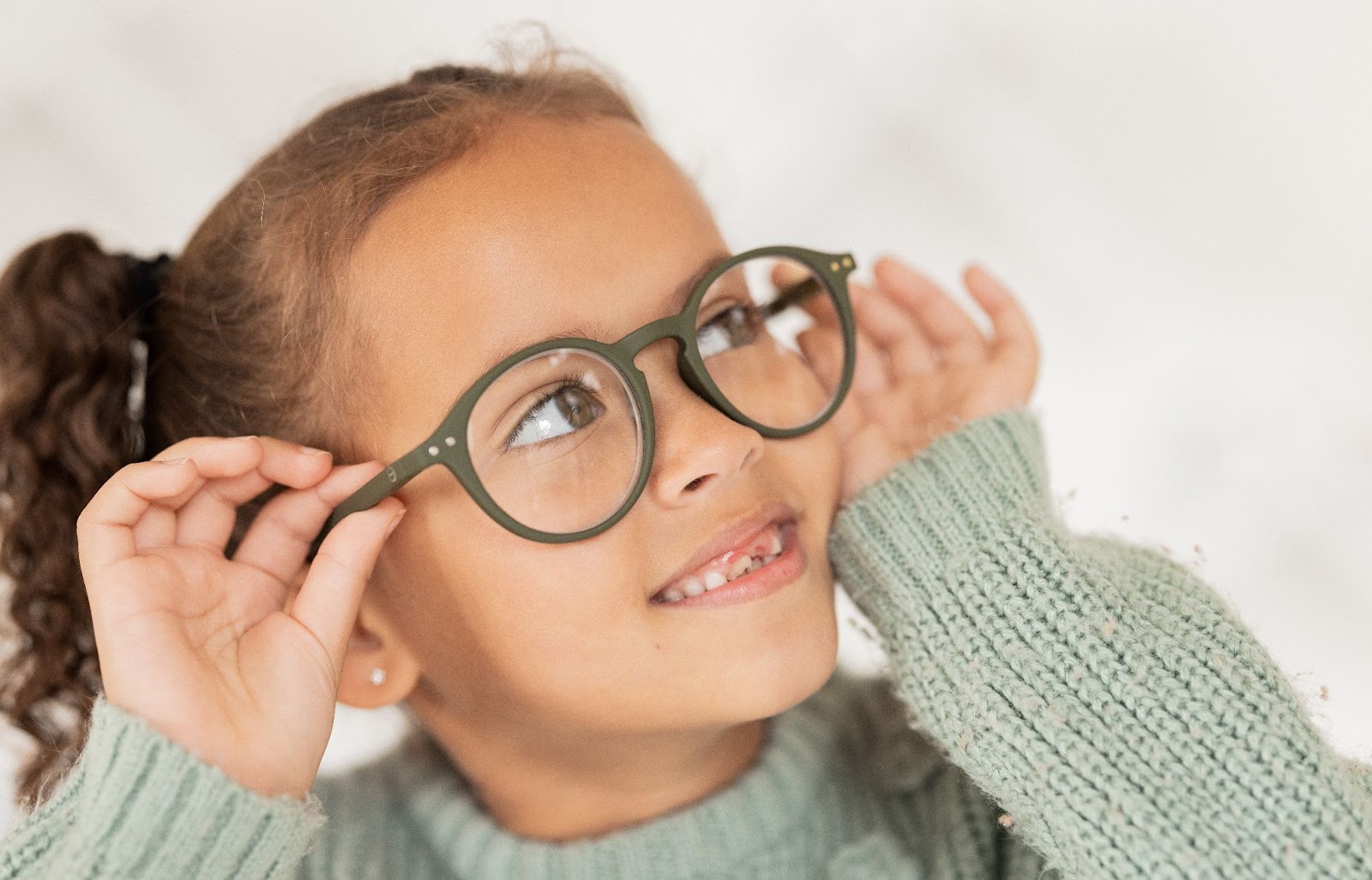 A child smiling while trying on a pair of eyeglasses.