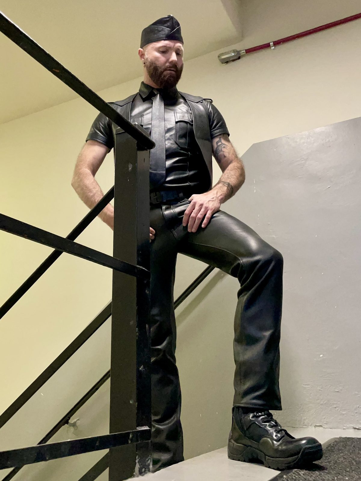 Rob Montana in a gay leather porn attire stroking his cock through his gay leather bdsm pants and posing on a stairwell