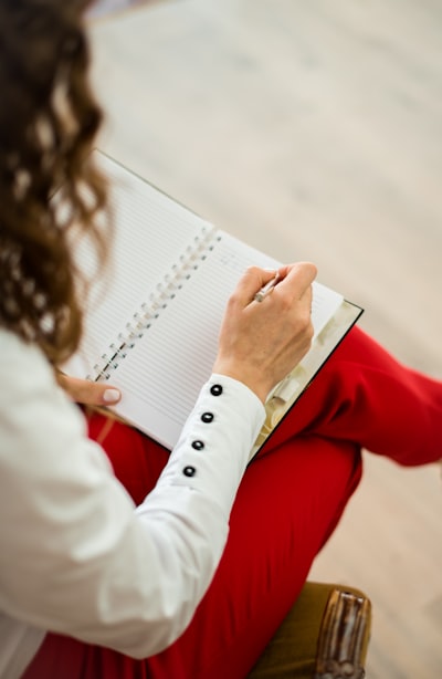 woman in white button down shirt and red pants, writing in journal