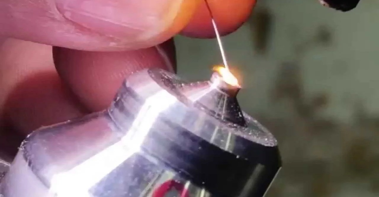 A close view of a wire being heated by a lighter flame, resulting in a spark.