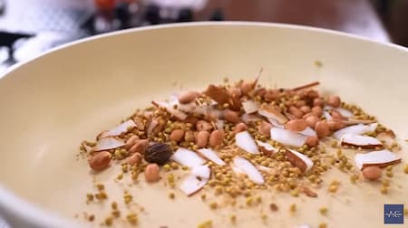 Peanuts, coconut, and spices being dry roasted in a pan.