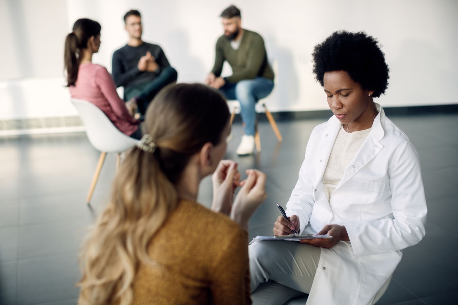  A female psychotherapist is taking notes as her female patients open up.