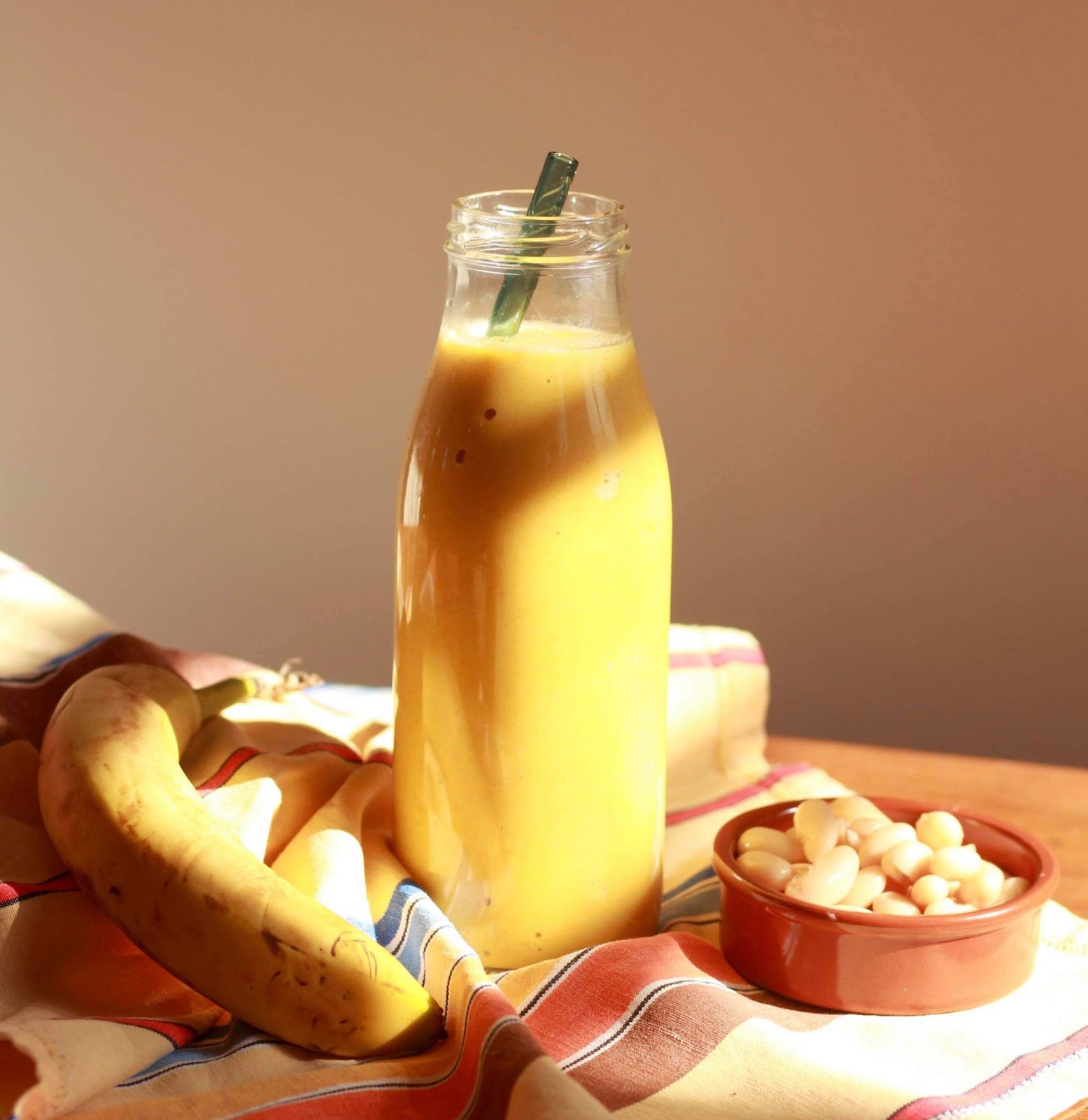 Protein smoothie with mango, ginger, and white beans in a glass bottle with a reusable straw, accompanied by white beans and bananas.