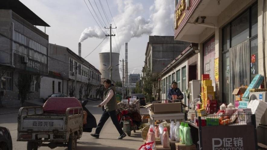 Guohua Power Station, a coal-fired power plant, operates as people sell items on a street in Dingzhou, Baoding, in the northern China's Hebei province, Friday, Nov. 10, 2023