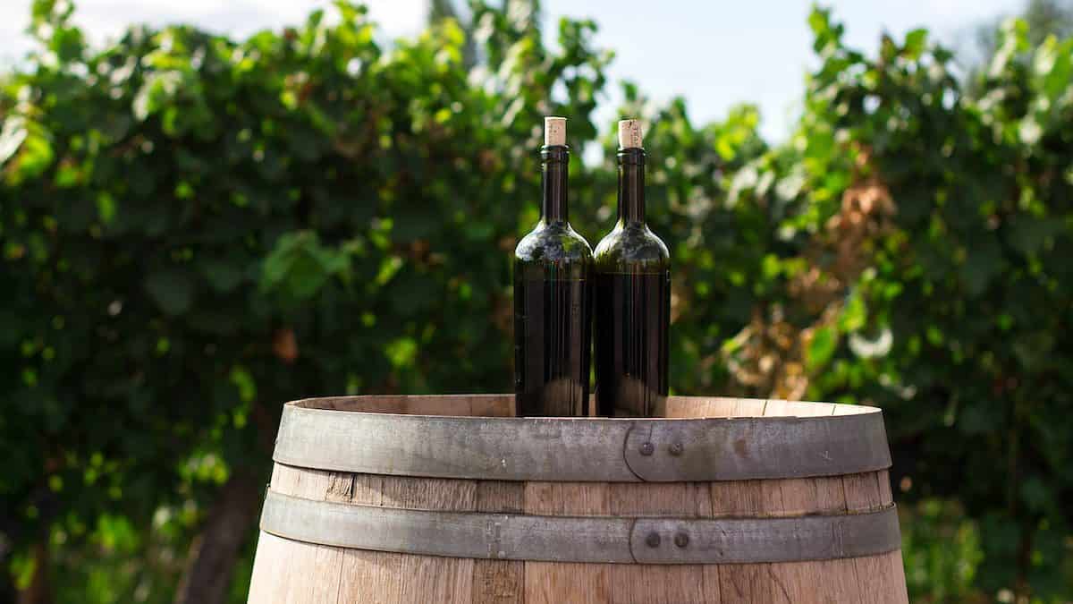 two black glass bottles on the top of the brown wooden barrel