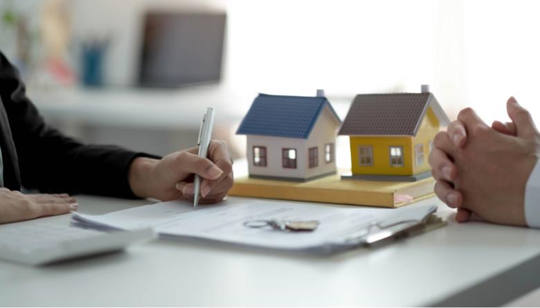 people signing paper next to two houses