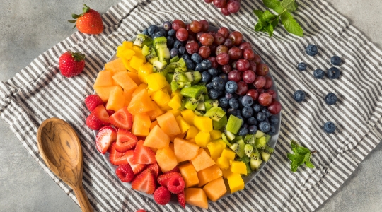 fraises, cantaloup, mangue, kiwi, bleuets et raisins dans une assiette sur un napperon rayé fris et blanc. 