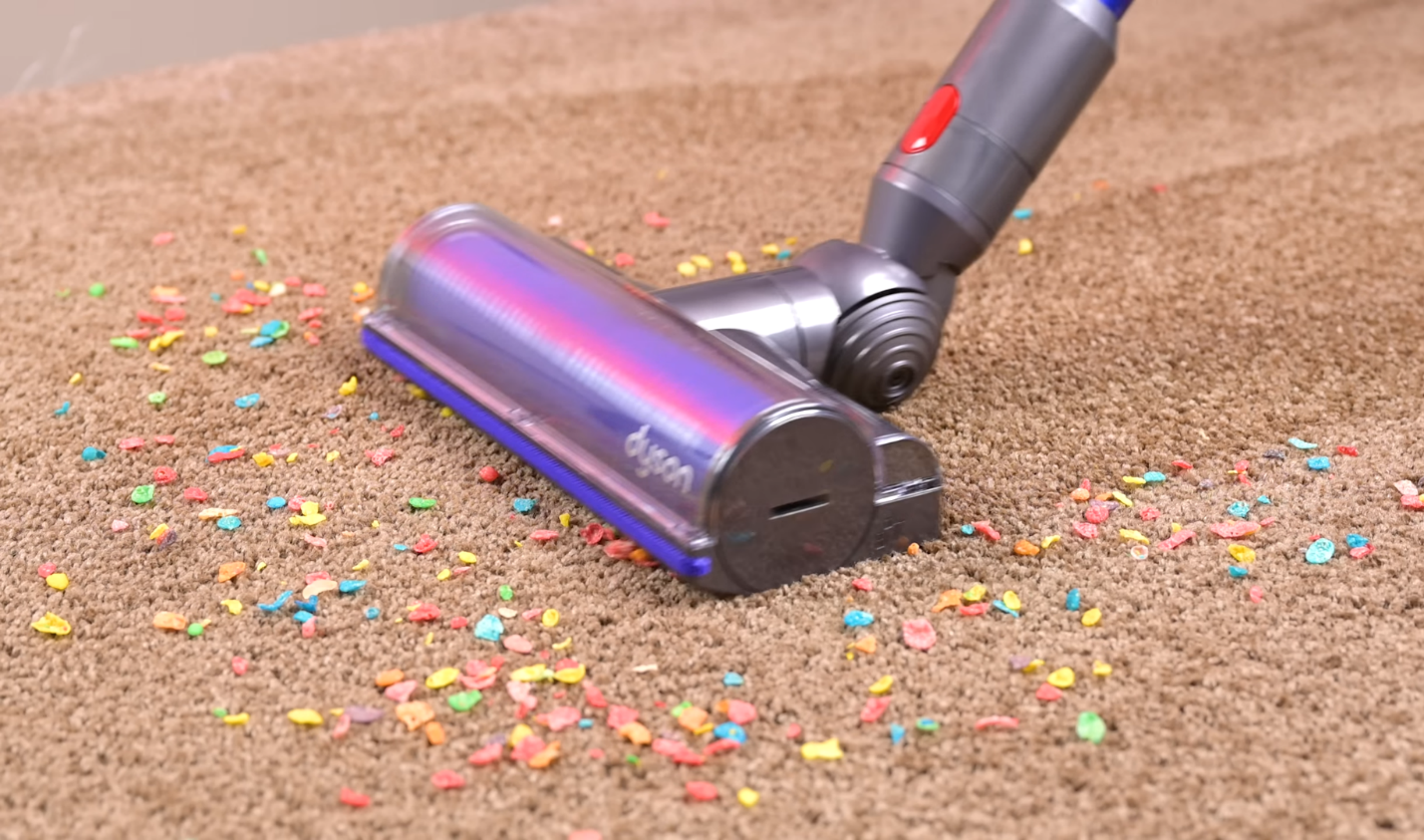 Dyson V11 vacuum in the process of cleaning up multicolored cereal pieces from a beige carpet