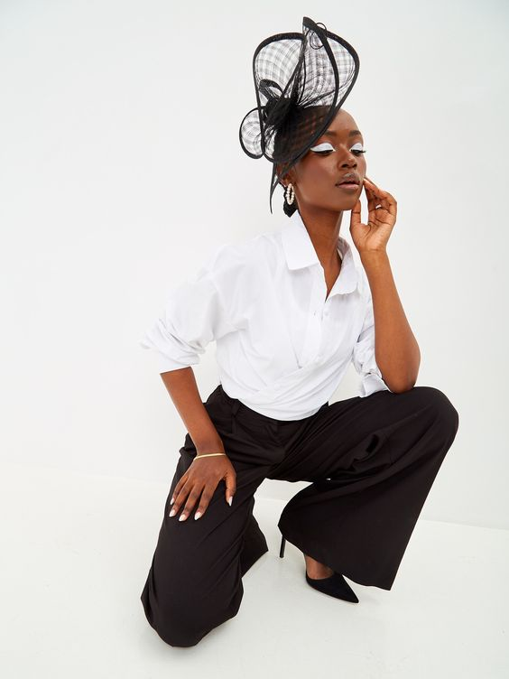 Picture of a lady rocking a tailored pants and white shirt matching it with her fascinator hat. 