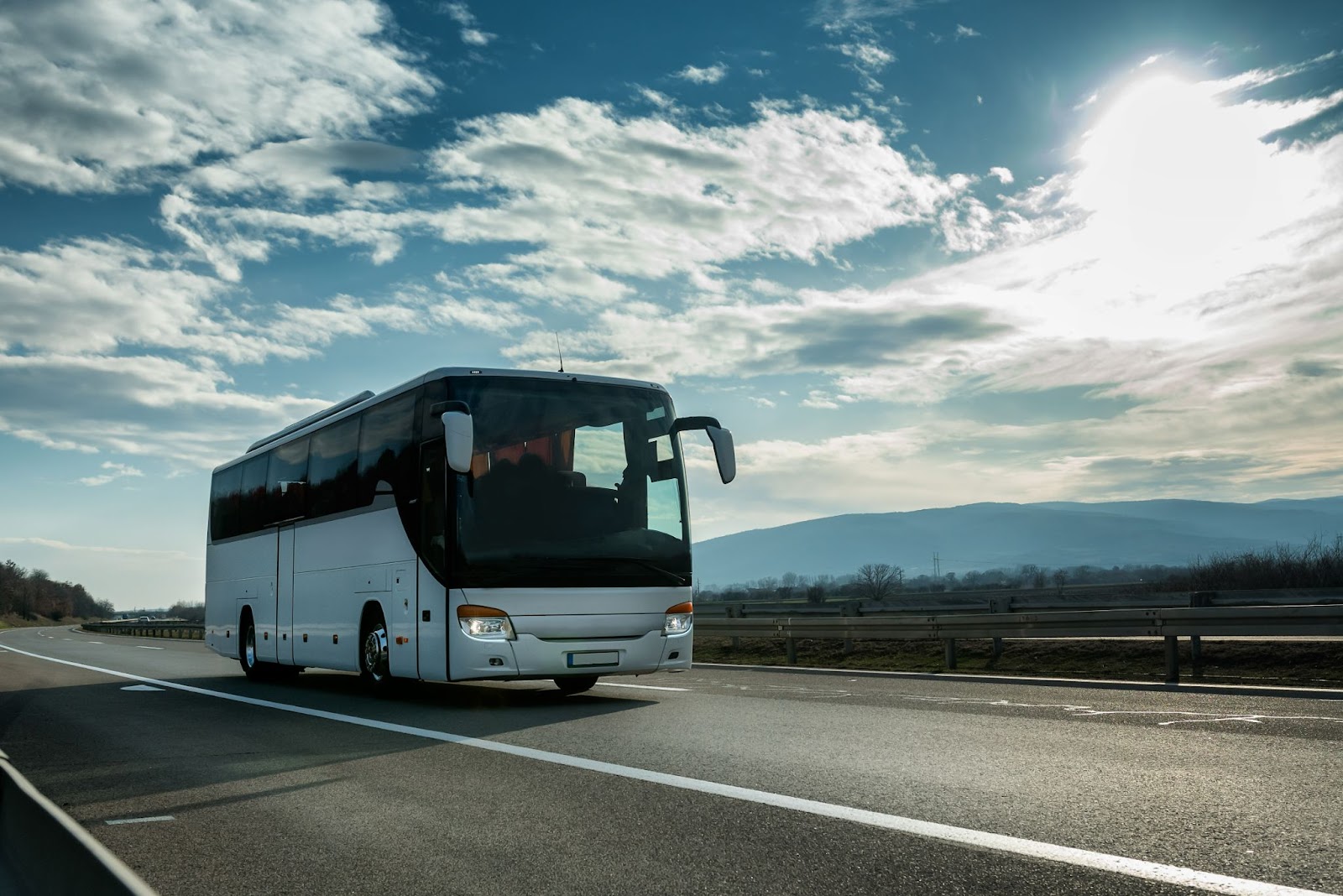 Ônibus de viagem em estrada vazia, céu azul com diversas nuvens brancas.