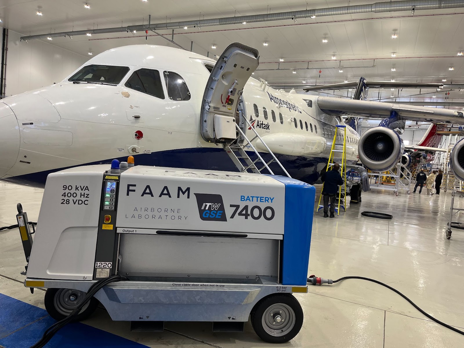 An electric ground power unit in front of a large blue and white research aircraft which is parked in a hangar.