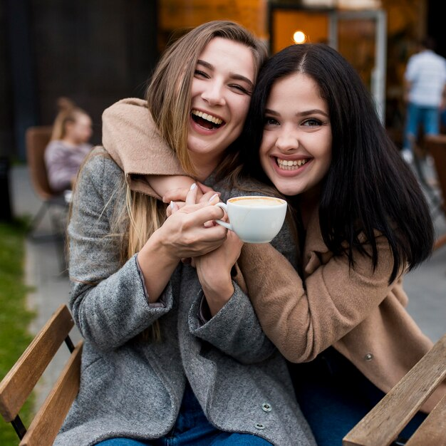 Woman holding a coffee cup receives a hug from her friend. 