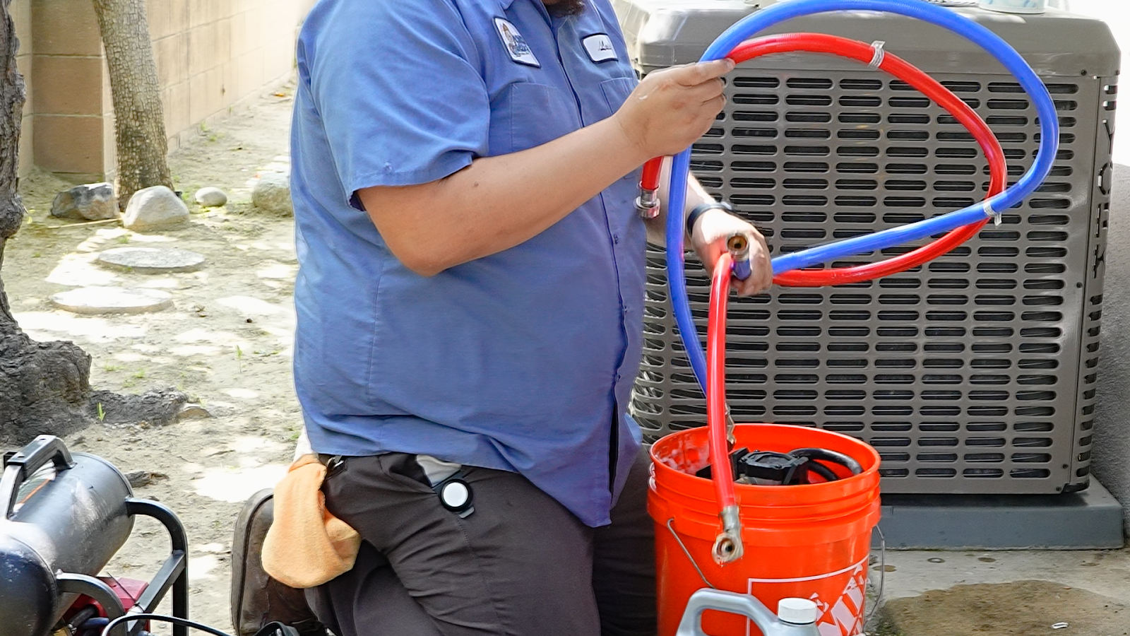 The image shows a Monkey Wrench Plumbing, Heating & Air technician kneeling down preparing equipment required for a tankless water heater flush. 